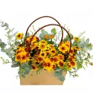 Basket of yellow and orange chrysanthemums and eucalyptus leaves with brown handles.