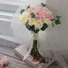 Pink and white roses and carnations in a bridal bouquet with a white ribbon.