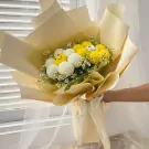 A bouquet of white and yellow chrysanthemums with tiny flowers, wrapped in pale yellow paper.