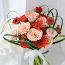 A bouquet of peach roses and orange gerbera daisies with green foliage.