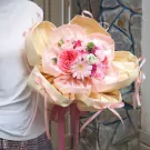 A bouquet of pink and cream flowers with delicate yellow and pink wrapping, tied with ribbon.