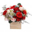 A wooden box filled with red roses, carnations, and hydrangeas.