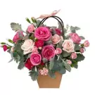 Basket of pink and red roses with greenery, tied with a pink ribbon.