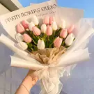 Hand holding a bouquet of pink and white tulips wrapped in white and brown paper with a sheer ribbon.
