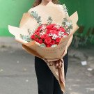A bouquet of red roses and baby's breath wrapped in brown paper with "Gorgeous You" text.