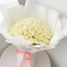 A large bouquet of white roses wrapped in white paper with a pink ribbon.