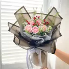 Pink roses, baby's breath, and red berries in a bouquet wrapped in black and grey paper with white ribbon.