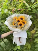 Bouquet of sunflowers and purple star flowers, wrapped in white paper.