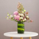 A floral arrangement of pink and white flowers in a green glass vase on a white table.