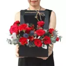 Woman holding a black box with red roses, carnations, and thistles.