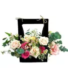 Black basket with pastel roses, carnations, and other flowers and greenery.