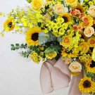 A large bouquet of yellow flowers, including sunflowers, roses, and orchids, with a pink ribbon.