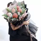 A bouquet of brown peonies with baby's breath and eucalyptus, wrapped in black and pink paper.