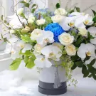 White orchids, roses, and blue chrysanthemums in a striped hatbox.