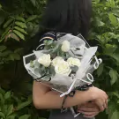 A bouquet of white roses with eucalyptus, wrapped in white paper and black ribbon.