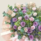A bouquet of purple and pink roses, hydrangeas, eucalyptus, and filler flowers.