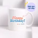 White ceramic mug with "Happy Birthday! to NAM" in coral and blue text.