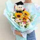 Graduation bouquet with sunflowers, carnations, daisies, and a teddy bear in a graduation cap.