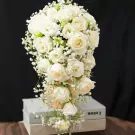 Cascading bouquet of white roses and baby's breath, presented in a vase on top of books.