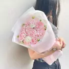 Pink roses in a bouquet wrapped in white and pink paper, held by a woman.