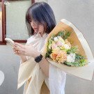 A woman in a white shirt holds a pastel flower bouquet, looking at her phone.