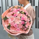 Pink roses and carnations arranged in a bouquet with light pink paper and ribbon.