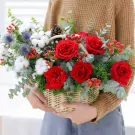 A hand-woven basket overflowing with red roses, cotton, berries, and greenery.