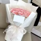 A bouquet of pink roses wrapped in white paper and tied with a white ribbon.