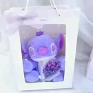 Purple Stitch plush toy with a crown and a bouquet of mini flowers in a white gift bag.