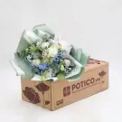 Bouquet of white roses, blue hydrangeas, and baby's breath in green paper on a brown box.
