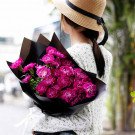 Woman in straw hat holding bouquet of deep pink carnations wrapped in black paper.