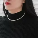 Close-up of a woman wearing a delicate pearl necklace and a black turtleneck.
