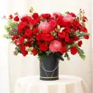 Red roses, pink peonies, and red carnations in a black bucket on a table.