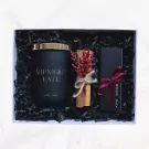 Gift set with a black candle, cinnamon sticks, dried flowers, and a black box with a red ribbon.