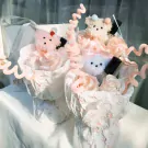 Bouquet of pink and white plush teddy bears nestled in paper flowers with decorative pink swirls.