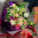 A bouquet of pink, white, and purple flowers with daisies, wrapped in purple paper.