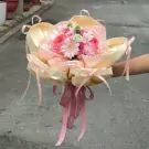 Pink and cream flowers with satin ribbons arranged in a bouquet.