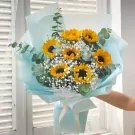A bouquet of sunflowers and baby's breath wrapped in light blue paper.
