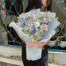 A woman holds a pastel blue and pink mixed flower bouquet.