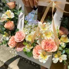 A bouquet of peach roses, white and yellow lilies, with a blue butterfly decoration in a white box.