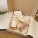 A gift box with a candle, glass jar of dried flowers, and a note.