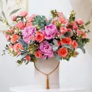 Pink and coral peonies and roses in a light grey hatbox with a gold tassel.