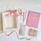 Pink and white gift set for women including a notebook, pens, a flower lollipop, a candle, and a "Happy Women's Day" card.