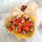 Bouquet of orange roses and pink carnations with eucalyptus, wrapped in light yellow paper.