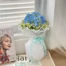 Bouquet of blue hydrangeas and white flowers wrapped in white paper with a light blue ribbon.