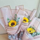Three bouquets of sunflowers and greenery wrapped in pink and gold paper, tied with blue ribbon.