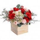 A floral arrangement in a wooden box, featuring red roses, pink roses, hydrangeas, and carnations.