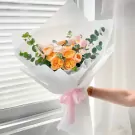 A bouquet of peach and cream roses with eucalyptus, wrapped in white paper and tied with a pink ribbon.