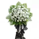 White flower arrangement with green leaves and black ribbon on a wooden stand.