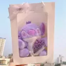 Purple Stitch plush toy with a crown, holding a mini bouquet of purple flowers in a white gift box with a ribbon.